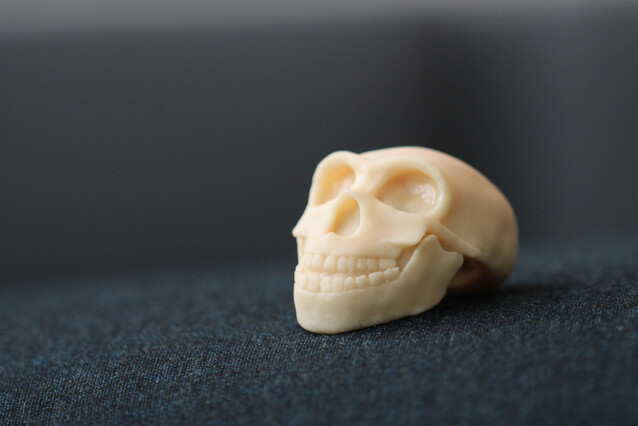 A small yellowish plastic skull sits on a dark grey surface.