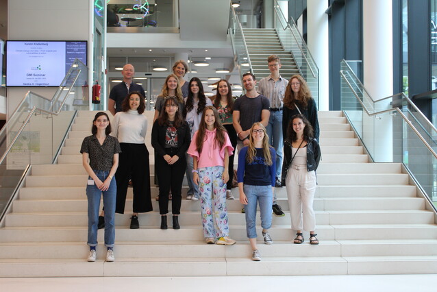 A group of young people stands on a white staircase, they are smiling and looking at the camera.