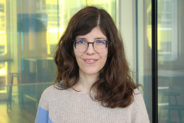 A young woman with glasses and long dark hair smiles at the camera.